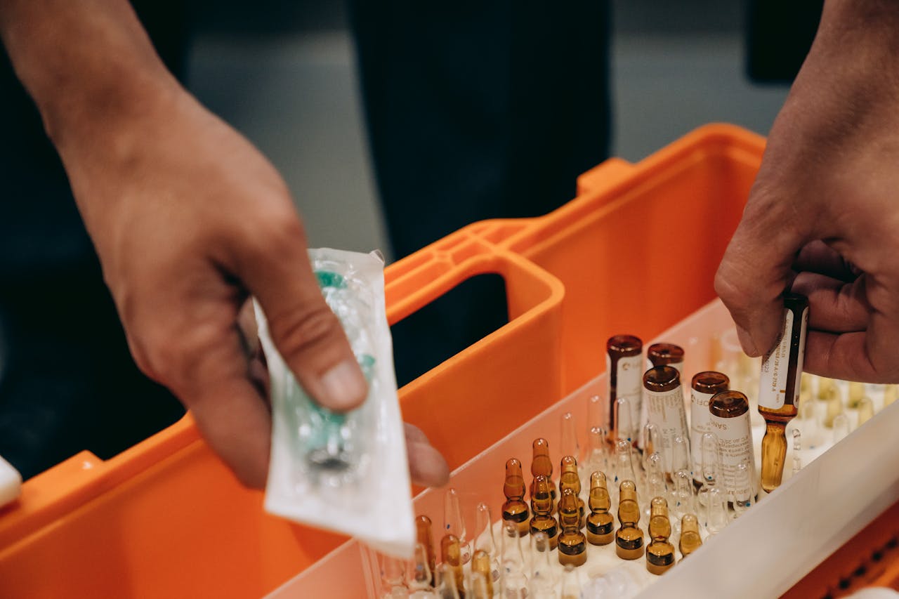 about-us Close-up of hands organizing vials and syringe in a medical first aid kit, emphasizing emergency readiness.